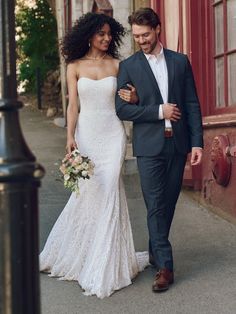 a bride and groom are walking down the street in their wedding attire, holding hands