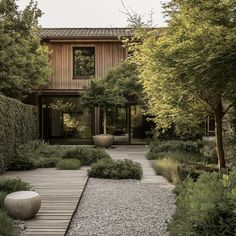 a garden with gravel, rocks and trees in front of a wooden house on the other side