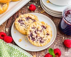 two raspberry crumb cookies on a plate next to fresh raspberries