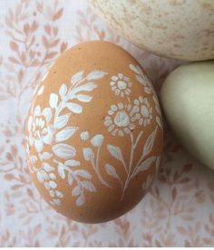 an orange painted egg sitting next to two white eggs on a pink and white tablecloth