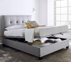 a bed with an open drawer underneath it in a white room next to a window