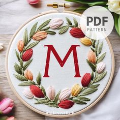 a hand embroidered monogram with flowers and leaves in the hoop on top of a wooden table