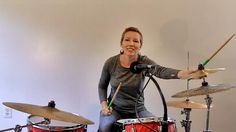 a woman sitting on top of a red drum set next to a microphone and drumstick