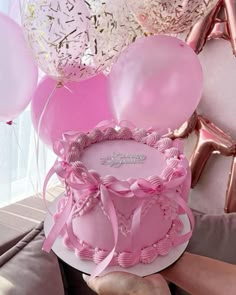 a person holding a pink birthday cake with balloons in the shape of heart on top