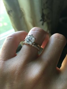 a woman's hand with a diamond ring on her finger and a window in the background