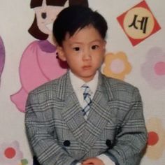 a young boy wearing a suit and tie in front of a wall with children's pictures