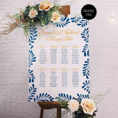 a wedding seating chart with flowers and greenery on the back side, against a white brick wall