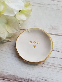 a white and gold plate with the word mom written on it next to some flowers