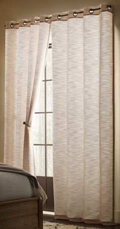 a bed sitting next to a window covered in white curtains