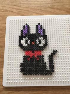 a beaded cat sitting on top of a white plate with black and purple beads