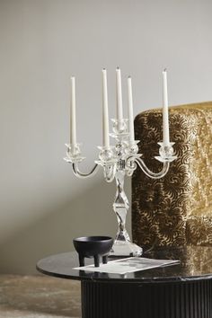 a candle holder with five candles on it and a chair in the backround