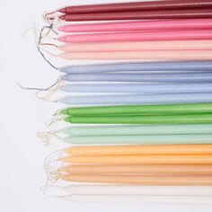 many different colored candles are lined up on a white surface with string tied around them