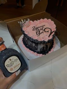 a pink and black birthday cake in a box with a bottle of booze next to it