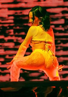 a woman in yellow outfit on stage with her legs spread out and hands behind her back