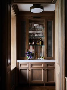 a kitchen with wooden cabinets and white counter tops, along with wine glasses on the shelves