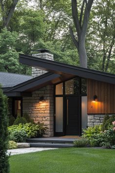 a small house with a black roof and stone walls, surrounded by lush green trees