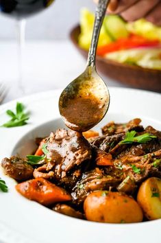 a person is spooning some food out of a bowl with potatoes and carrots