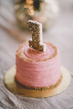 a pink cake with a gold number one on it's top and the word i spelled by cristine