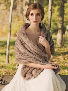 a woman is sitting on a bench wearing a fur shawl and earrings, in the woods