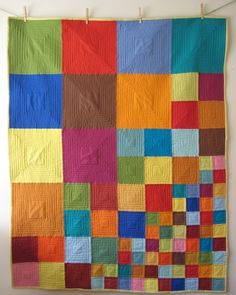 a multicolored quilt hanging on a clothesline in front of a white wall