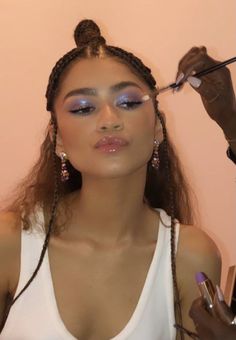 a woman is getting her make up done in front of a pink wall with scissors