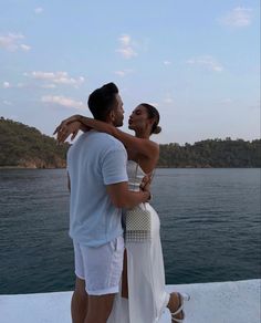 a man and woman standing on the edge of a boat looking at each other with their arms around one another