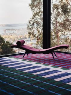 a pink chaise lounge chair sitting on top of a colorful rug in front of a window