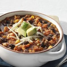 a white bowl filled with chili, beans and avocado on top of a blue napkin