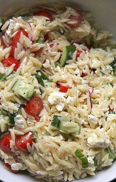 a white bowl filled with pasta salad and cucumber, tomato, and feta cheese