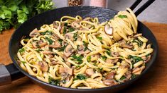 pasta with mushrooms and spinach in a skillet on a wooden table next to a plant