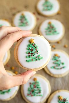 a person holding a decorated christmas tree cookie in front of some cookies on a table