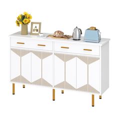 a white cabinet with gold trim and geometric designs on the doors, two tea kettles and a potted sunflower