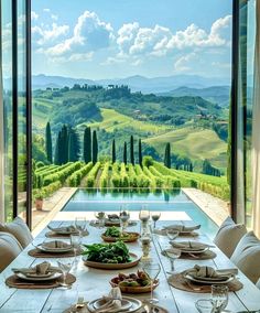 a dining table with plates and place settings in front of an outdoor pool overlooking the countryside