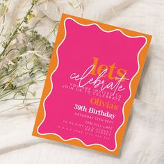 an orange and pink birthday party card on a white sheet with flowers in the background