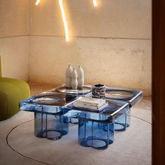 two blue tables with vases on them in front of a yellow chair and wall