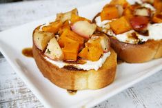 two pieces of bread topped with fruit and cream on top of a white square plate