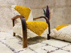 a chair with yellow and white cushions sitting on top of a rug next to a pillow