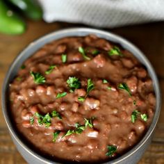 a metal bowl filled with beans on top of a wooden table next to green peppers