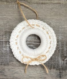 a white crocheted wreath hanging on a wooden surface with twine and rope