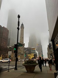 people are walking down the street in front of tall buildings on a foggy day