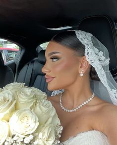 the bride is sitting in her car holding a bouquet of white roses and wearing a tiara