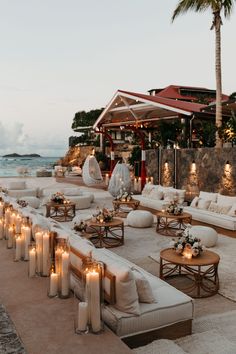 an outdoor seating area with candles lit on the tables and couches near the water