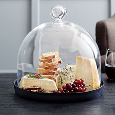 a platter with cheese, crackers and grapes under a glass dome