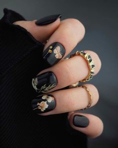 a woman's hand with black nail polish and gold rings on her fingers, decorated with flowers