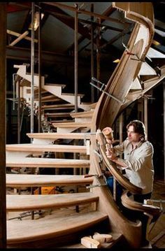 a man standing next to a spiral staircase in a building with wooden floors and handrails