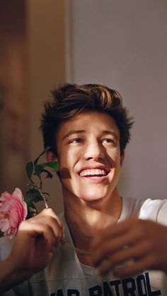 a young man is holding a flower and smiling