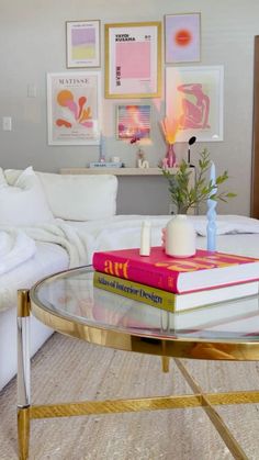 a glass table with books on it in front of a white couch and coffee table