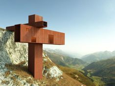 a wooden cross sitting on top of a hill next to a cliff side with mountains in the background