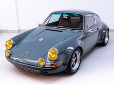 an old grey porsche sits parked in a white room with its lights on and the door open