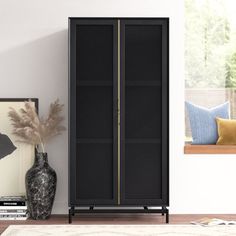 a black cabinet sitting in the corner of a living room next to a vase and pictures